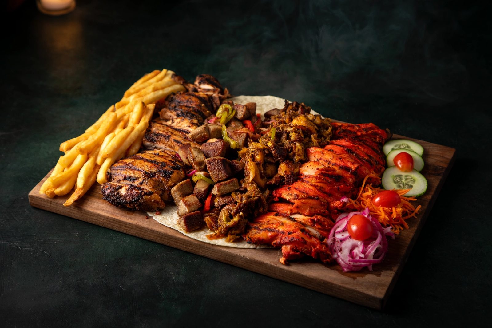 Mixed grill platter for two on a wooden board with kebabs, tikka and fries